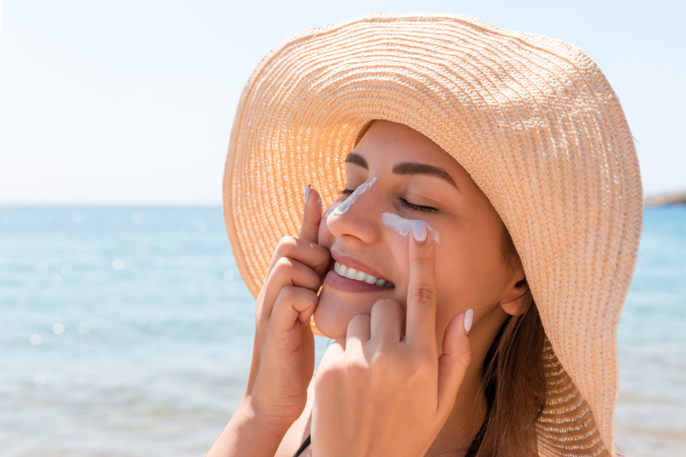 Smiling,Woman,In,Hat,Is,Applying,Sunscreen,On,Her,Face.